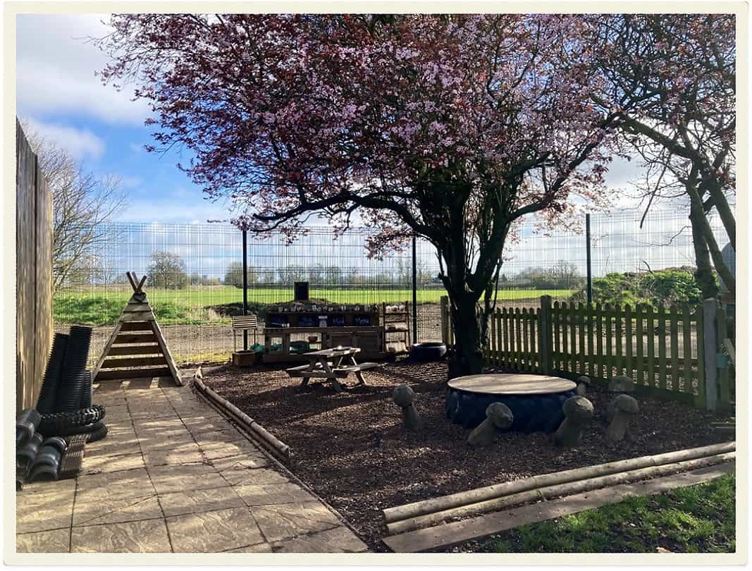Childcare outdoor play area with tree, seating, and fencing.