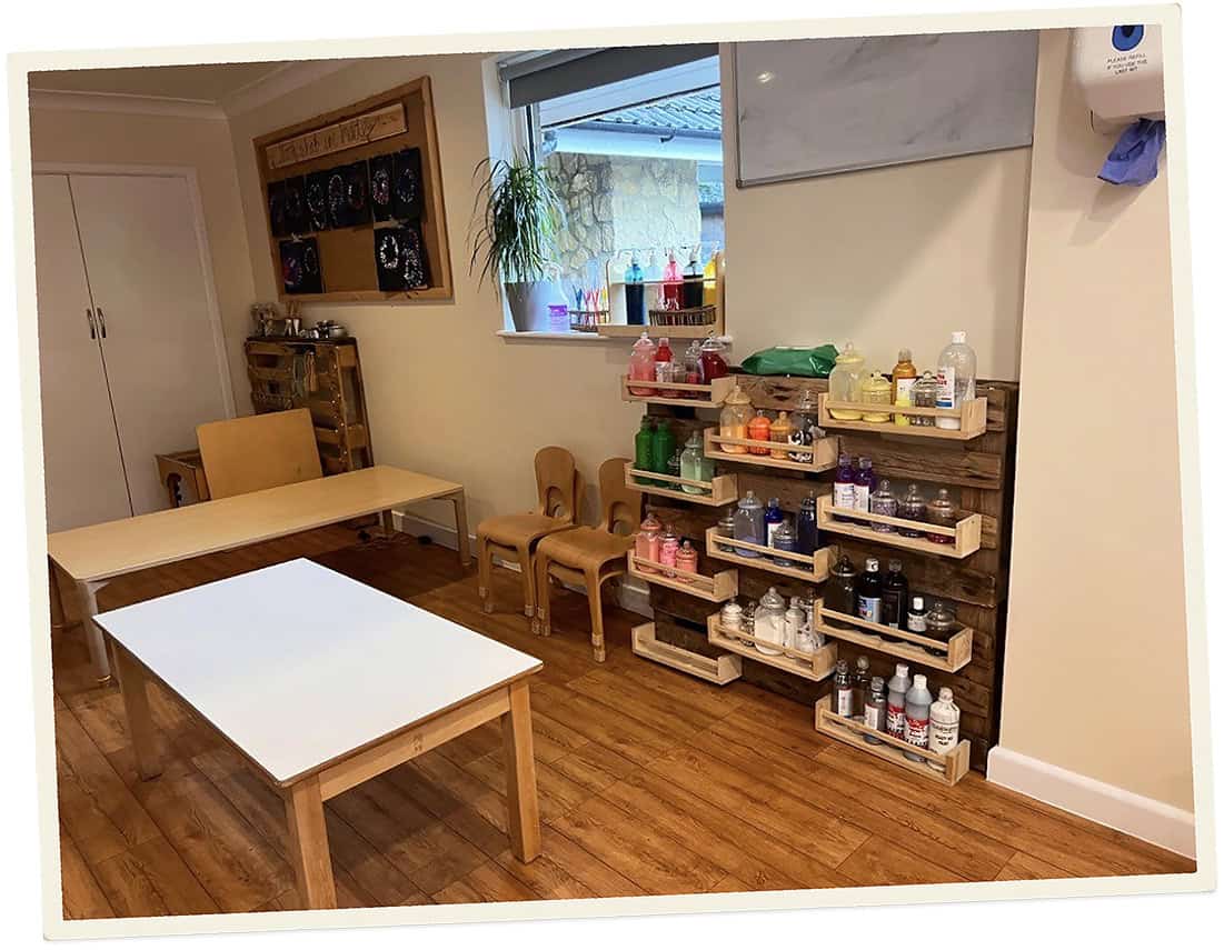Childcare room with tables, chairs, and shelves of supplies at Lancaster Lodge.