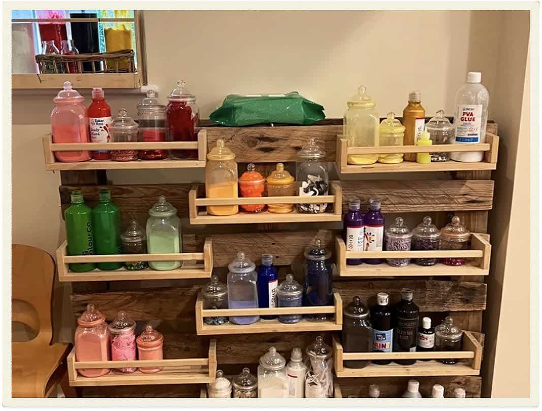 Colorful art supplies in organized bottles on wooden shelves at Lancaster Lodge Childcare.